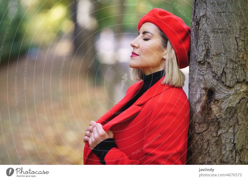 Verträumte Frau in der Nähe eines Baumes in einem Park verträumt Stil Mode Design feminin Outfit Herbst Bekleidung Kleidung Vorschein froh Augen geschlossen