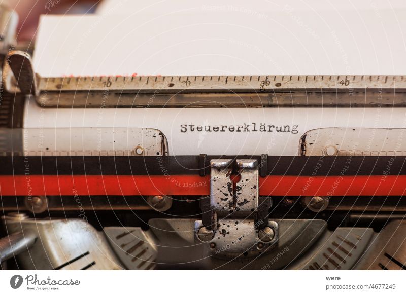 Das  deutsche Wort Steuererklärung geschrieben mit einer alten mechanischen Schreibmaschine mit rotem und schwarzem Farbband in schwarzer Farbe auf einem weißen Blatt Papier