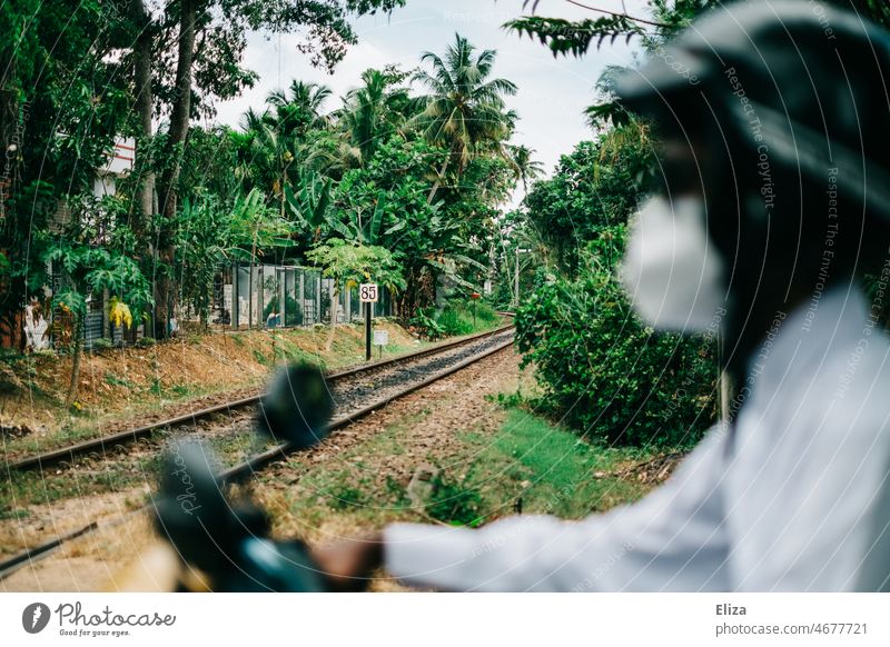 Mann mit Maske auf Roller vor Bahngleisen in Asien Verkehr Eisenbahn Mobilität Gleise Schienen Schienenverkehr