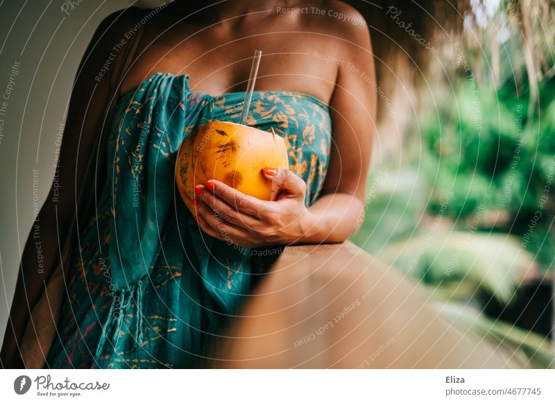 Frau in buntes Badetuch gewickelt hält eine King Kokosnuss mit Strohhalm in der Hand. Urlaub in den Tropen. Trinkkokosnuss Sommer tropisch Paradies exotisch