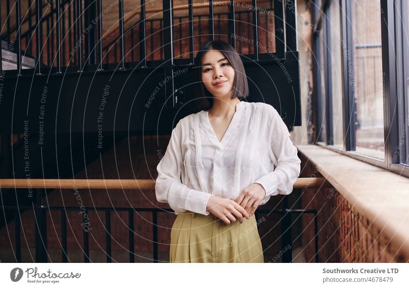 Porträt einer selbstbewussten erwachsenen chinesischen Frau, die sich lächelnd auf ein Geländer stützt und in die Kamera schaut asiatisch Business Mitte