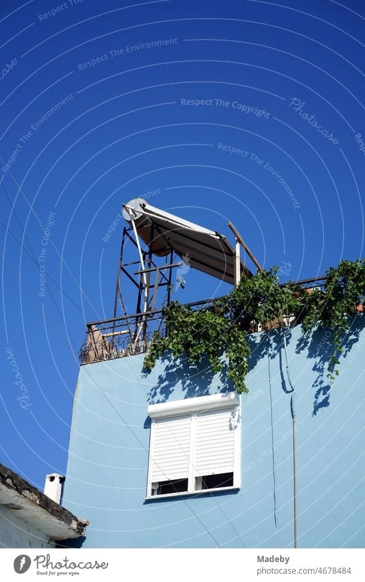 Solaranlage und Photovoltaik vor blauem Himmel im Sonnenschein auf der Dachterrasse eines hellblauen Wohnhaus im Sommer in der Altstadt von Foca am Ägäischen Meer in der Provinz Izmir in der Türkei
