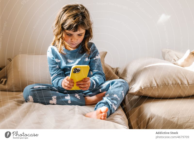 Mädchen im Pyjama spielt auf dem Smartphone Kind Kindheit Bett Schlafzimmer Videospiel spielen Zeitvertreib Morgen heimisch Appartement bezaubernd Barfuß flach