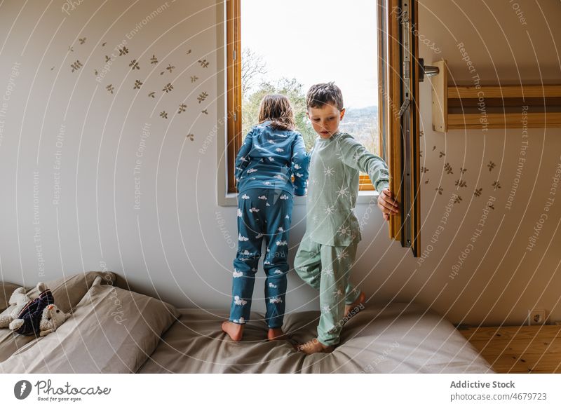 Geschwister im Schlafanzug schauen aus dem Fenster Geschwisterkind Kinder Kindheit beobachten neugierig Schlafzimmer Bett Pyjama Morgen freie Zeit Funktelefon