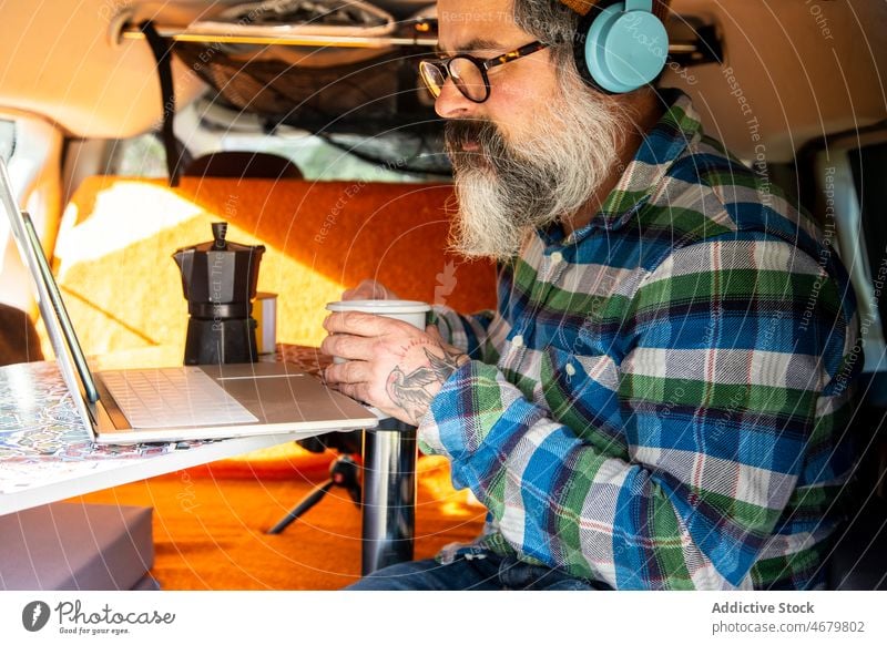 Älterer Mann schaut Video auf Laptop im Wohnmobil älter reif Kopfhörer Reisender Autoreise Kleintransporter Browsen zuschauen online Gerät Apparatur Netbook