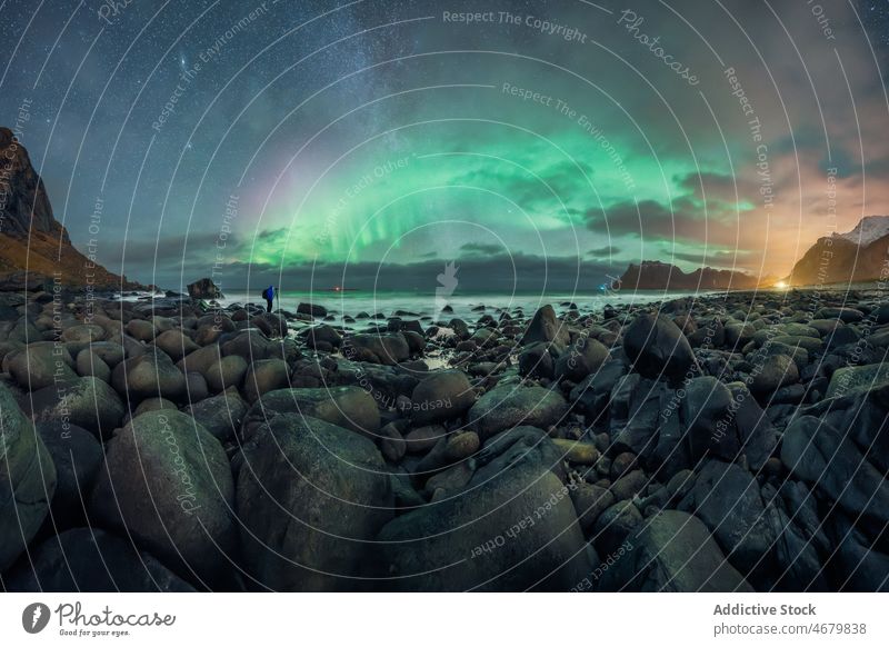 Anonymer Reisender, der vom felsigen Strand aus Polarlichter über dem Meer beobachtet Nordlicht MEER Natur sternenklar Himmel Ausflug bewundern Meeresufer