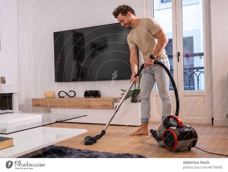 Mann staubsaugt Boden im Wohnzimmer Vakuum Raumpfleger Haushalt Hausarbeit Routine Vorrichtung ordentlich Arbeit heimwärts heimisch Sauberkeit modern FERNSEHER