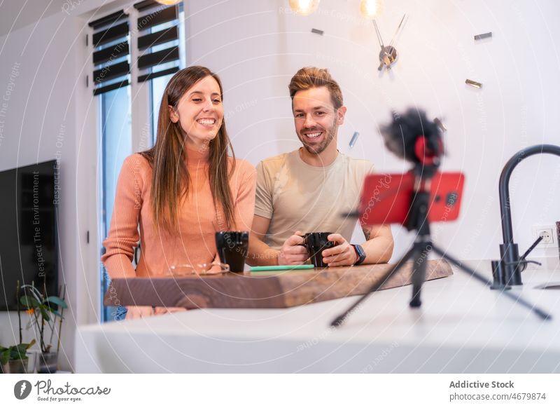 Fröhliches Paar nimmt Vlog auf, während es Kaffee trinkt Küche Blogger vlog Aufzeichnen Smartphone soziale Netzwerke Internet Koffein trinken Heißgetränk
