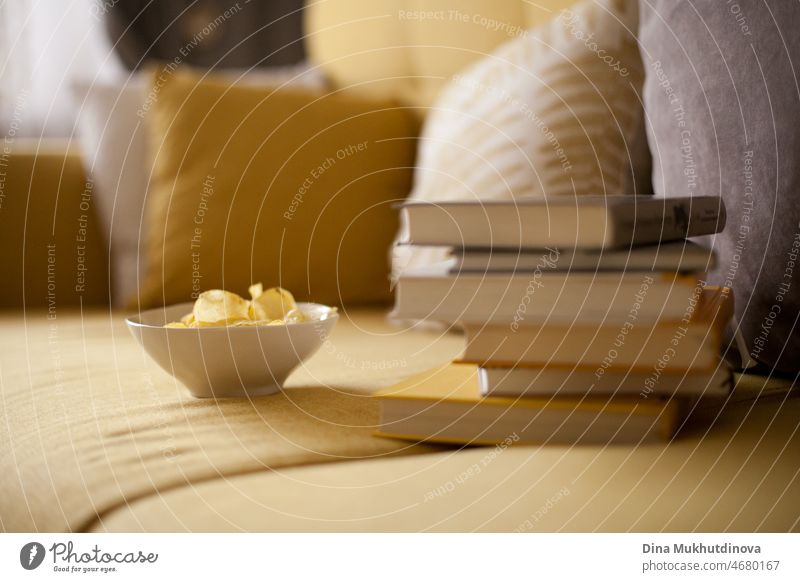 Ein Stapel Bücher und Kartoffelchips auf einer gemütlichen gelben Couch mit Kissen. Wohnen in einer Wohnung. Einfaches Leben. Lässiger Lebensstil der Millennials. Urlaub. Bildung.