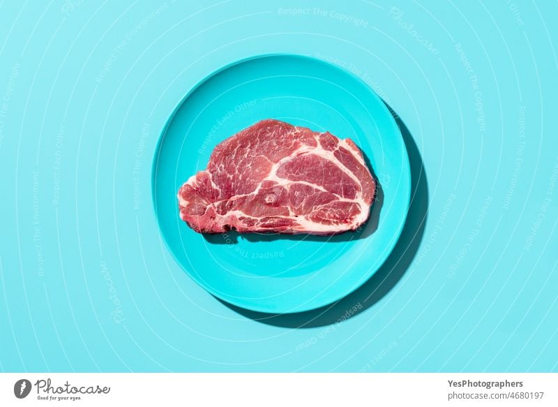 Rohes Schweinesteak auf einem Teller, Ansicht von oben. Steak isoliert auf blauem Hintergrund Barbecue grillen Rindfleisch Knochen hell Metzger hacken