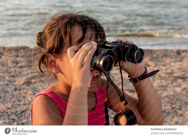 Gebräuntes Kleinkind mit braunen Haaren am Strand im Sommer schaut durch ein Fernglas Sonnenuntergang Kind niedlich Mädchen Glück Feiertag MEER Lächeln reisen