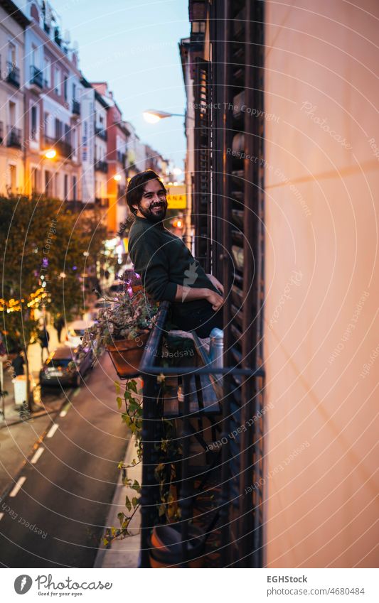Lässiger junger Mann lächelnd auf dem Balkon einer typischen Madrider Hausfassade in einer Straße Lächeln lässig gutaussehend 20s 30s Erwachsener Hintergrund