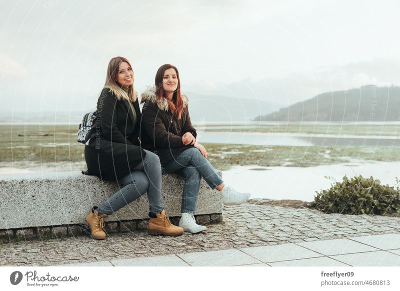 Zwei Freundinnen sitzen auf einer Bank Freunde Touristen Sitzen Landschaft Winter kalt Feuchtgebiet Galicia Spanien Sumpfgebiet betrachtend Windstille