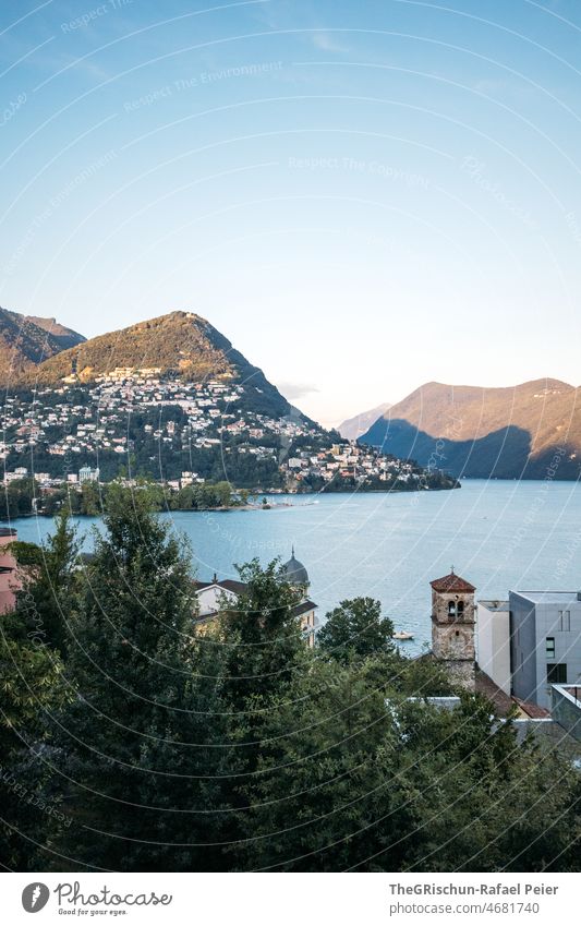 See vor Berge und Dorf in Abendstimmung Stimmung Schatten Berge u. Gebirge Lugano Luganosee Luganer See Kirche Aussicht Blauer Himmel Schweiz Tessin