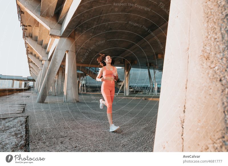 Junge multikulturelle Frau lächelt in die Kamera, während sie in der Stadt joggt, um vor dem Sommer Gewicht zu verlieren und einen definierten Körper zu bekommen. Laufen und Workout im Freien. Sonnenuntergang Szene mit jungen Athleten