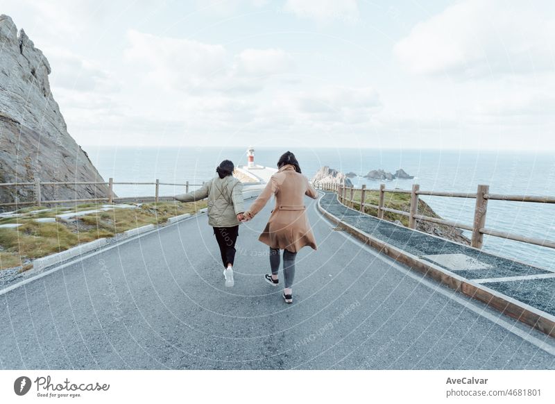Vintage-Filmbild von zwei jungen Frauen, die mit sanften Tönen auf einen Leuchtturm an der Küste zulaufen. Frühling Ambient Freiheit und Freiheit Konzepte. Freundschaft und Road Trip Vibes
