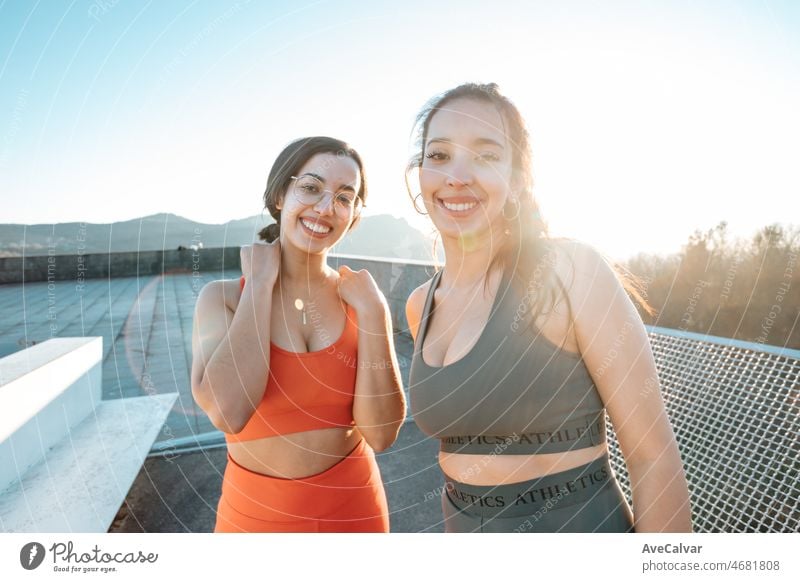 Zwei junge multikulturelle Frauen lächeln in die Kamera, bevor sie mit dem Training beginnen, um vor dem Sommer Gewicht zu verlieren und einen definierten Körper zu bekommen. Laufen und Workout im Freien. Sonnenuntergang Szene mit jungen Athleten