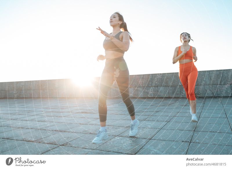 Zwei junge, multikulturelle Frauen joggen in einem städtischen Zug, um vor dem Sommer Gewicht zu verlieren und einen definierten Körper zu bekommen. Laufen und Workout im Freien. Sonnenuntergang Szene mit jungen Athleten