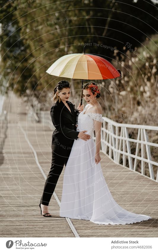 Lesbisches Paar umarmt sich während der Hochzeit auf einer Brücke Frauen Braut Park Umarmung Liebe Regenschirm lesbisch Zusammensein Jungvermählter elegant