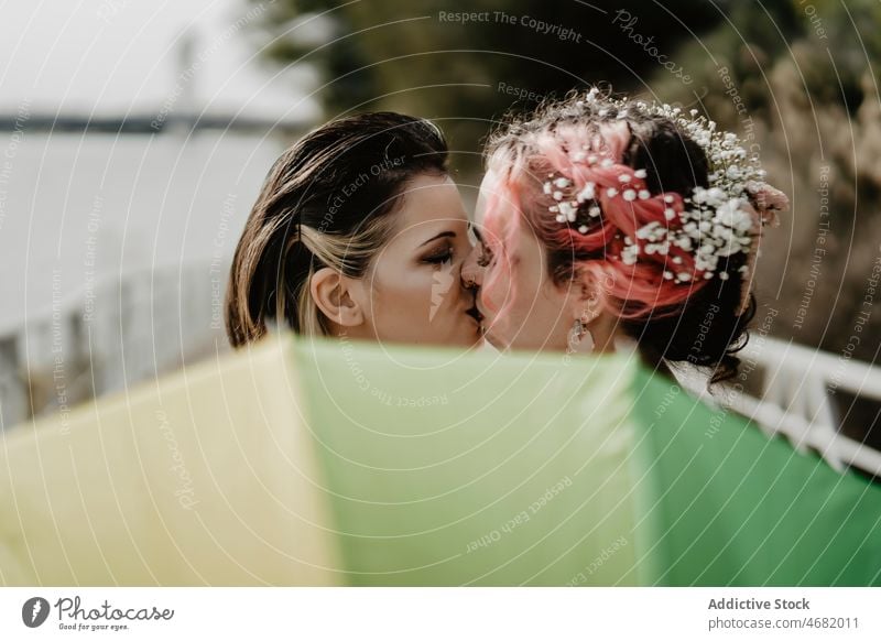 Bräute küssen sich während der Hochzeit hinter einem Regenschirm Frauen Kuss Braut Liebe lesbisch Paar Park feiern Zusammensein romantisch hochzeitlich Glück