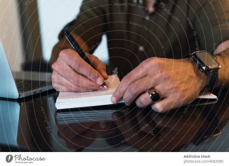 Anonymer Mann schreibt in ein Notizbuch neben einem Laptop zur Kenntnis nehmen Notebook Notizblock schreiben Arbeit Arbeitsplatz Erinnerung Aufgabe Netbook