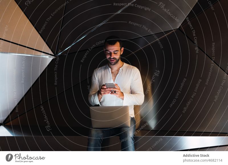 Mann mit Laptop, der in einem Studio auf seinem Smartphone surft futuristisch 3d Browsen Textnachricht Atelier modern Design online Internet männlich Typ