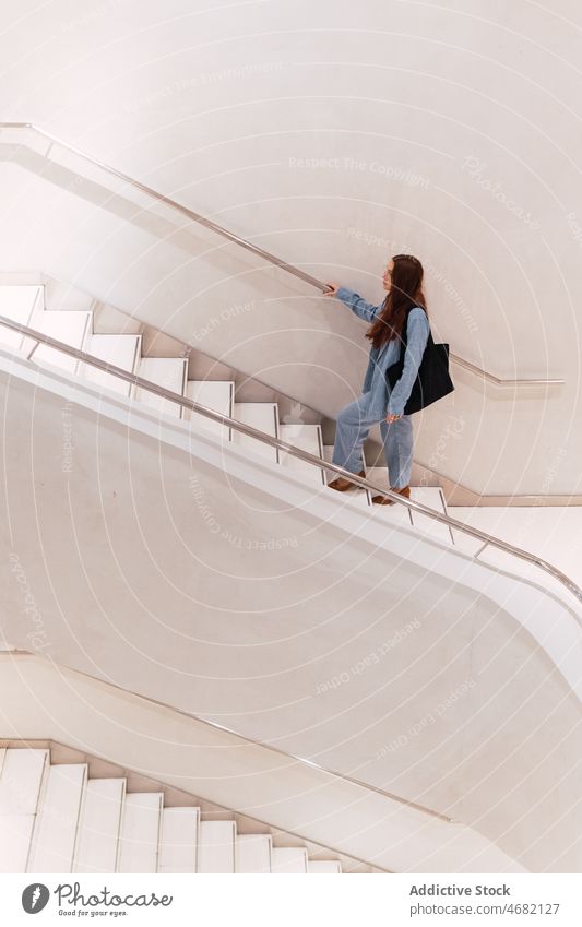 Unbekannte Frau auf der Treppe Treppenhaus nach oben elegant Stil Design Gang Saal Mode trendy Spaziergang Flur lange Haare Handtasche geräumig feminin Schritt
