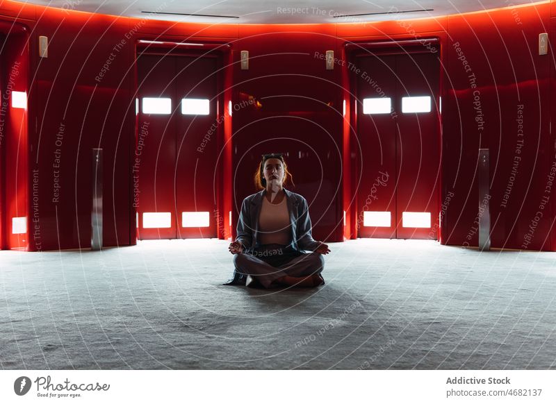 Meditierende Frau im Foyer mit Aufzügen Wandelhalle Fahrstuhl Lotus-Pose Zen heben meditieren Stressabbau obskur Design feminin glühen dunkel rot geräumig
