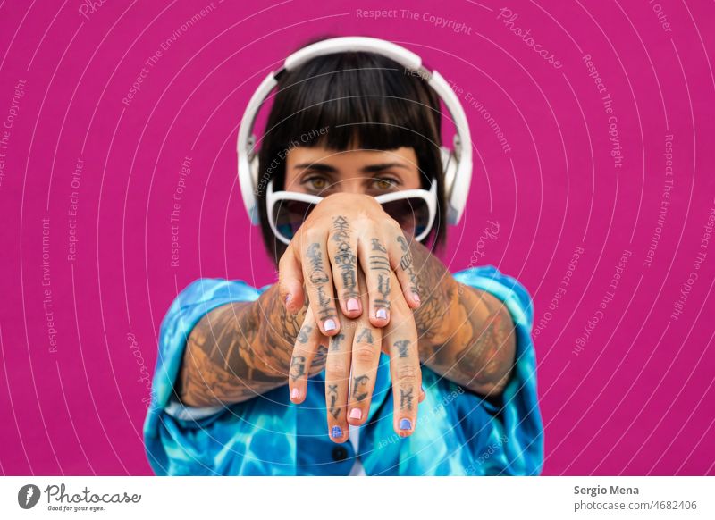 Attraktive Frau mit Kopfhörern zeigt die Tattoos auf ihren Händen auf einem rosa Hintergrund charismatisch brünett jung hell blau Hemd Atelier sexy Model hübsch