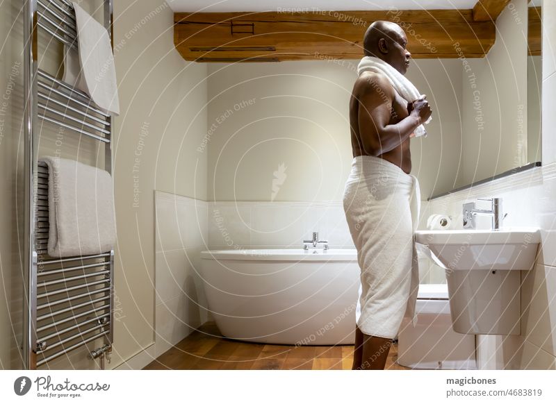Mann afrikanischer Abstammung, in ein Handtuch gewickelt, in einem modernen Badezimmer Erwachsener Afrikanisch Afro-Look Amerikaner Hintergrund Schönheit