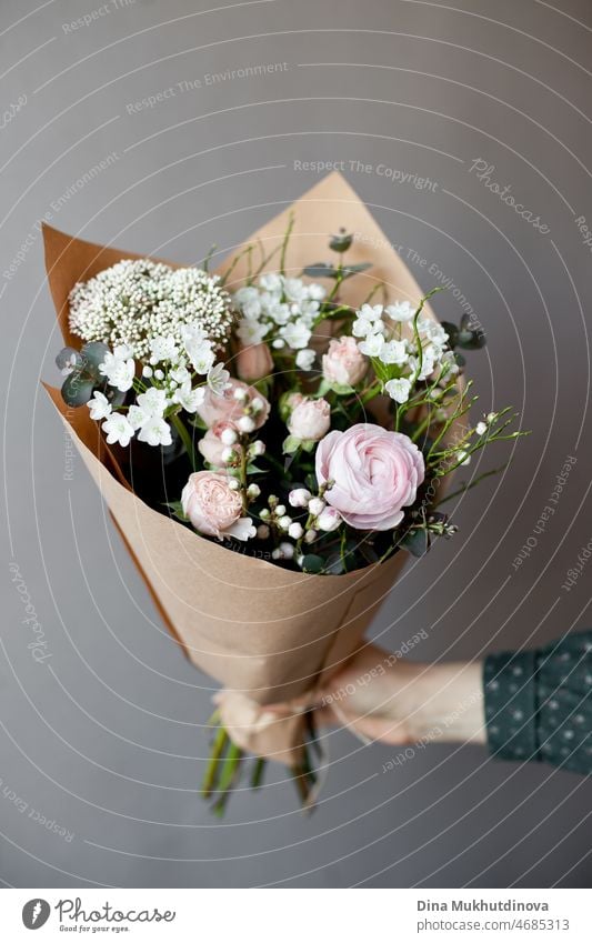Hand hält Blumenstrauß von rosa und weißen flowerson Holztisch im Blumenladen. Floristik und Verkauf von Blumen kleines Geschäft. Rosa frischen Frühling blumigen Hintergrund mit Kopie Raum auf hellgrauem Hintergrund.