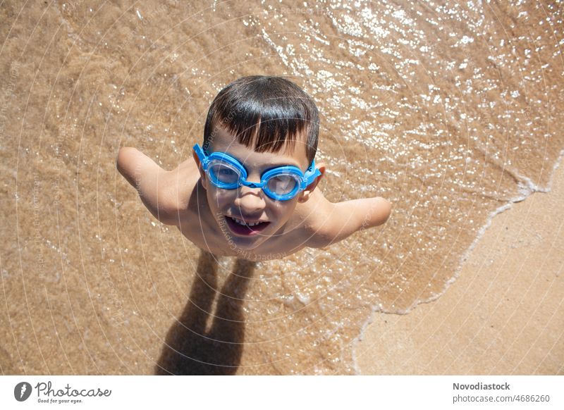 Porträt eines kaukasischen 6-jährigen Jungen am Strand, der eine Schwimmbrille trägt, Bild von oben aufgenommen, Sommerferienkonzept Durchnässen Draufsicht