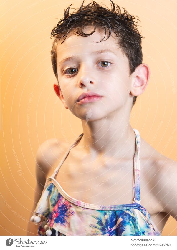 Porträt eines 6-jährigen Jungen, der ein Bikini-Oberteil trägt, isoliert auf einem hellen Hintergrund Bikini Top männlich niedlich Mode bisexuell Sommer schön