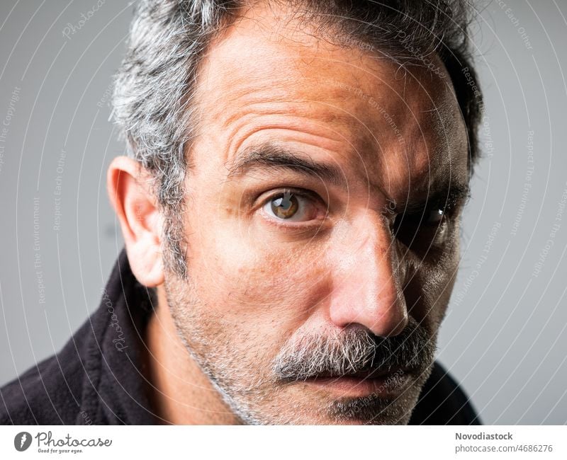Porträt eines 45-jährigen kaukasischen Mannes, der mit einer lustigen Geste in die Kamera schaut, mit einem Schnurrbart, isoliert auf grauem Hintergrund