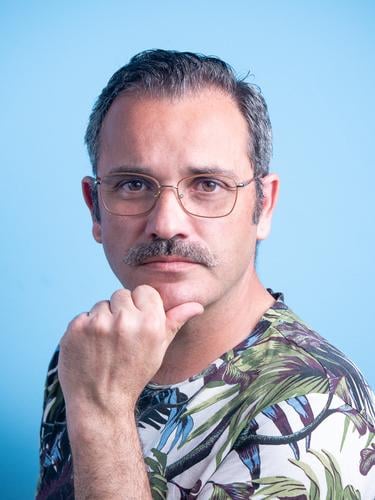 Porträt eines 45-jährigen kaukasischen Mannes mit Schnurrbart, der in die Kamera schaut, mit Brille und Freizeitkleidung, isoliert auf blauem Hintergrund