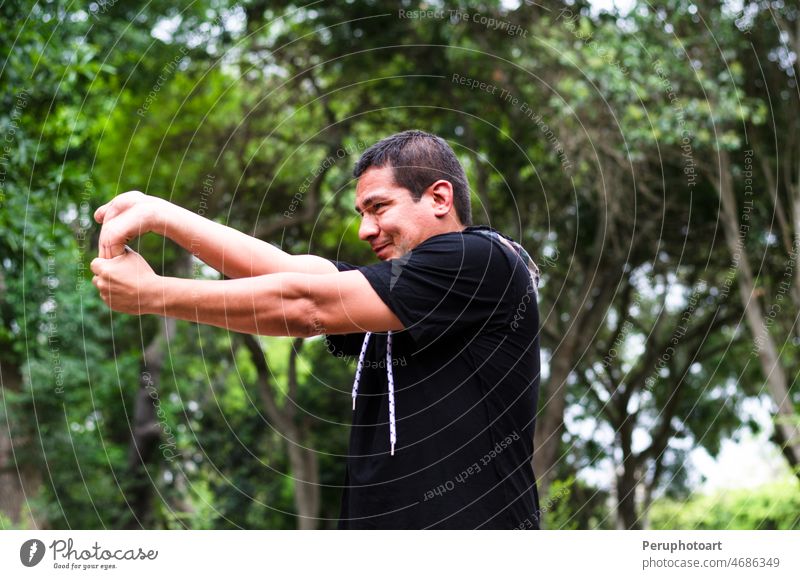 Junger Peruaner, der sich vor dem Training durch Strecken der Arme aufwärmt. Mann jung trainiert. Herz Gesicht Person Sport Fitness Sommer Natur Sonne Übung