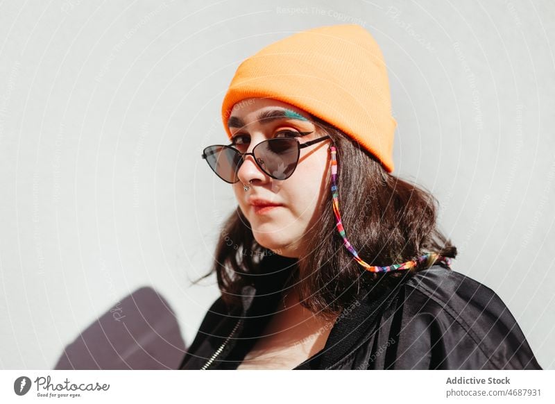 Stylische Frau mit Sonnenbrille und Perlen Stil Design Accessoire informell Wulst anketten Stilrichtung Mode Hut Kopfbedeckung Straße Großstadt trendy Wand