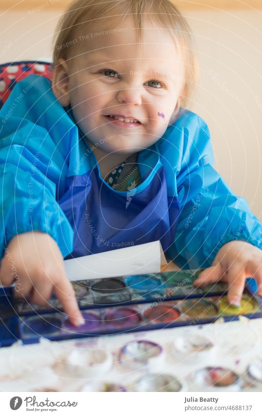 18 Monate altes Kleinkind, das mit zwei Händen gleichzeitig Aquarelle malt, während es im Hochstuhl sitzt packen Halt Pinsel Entwicklungsmeilenstein