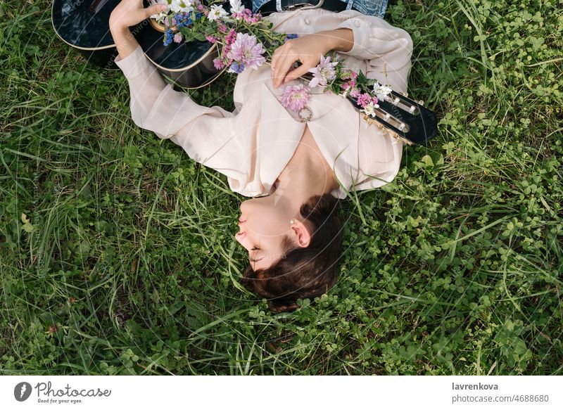 Junge Frau liegt im Gras und hält eine mit Blumen bedeckte Gitarre im Freien Musiker Person Spielen Instrument Beteiligung Strumming Lifestyle Gesang Klang