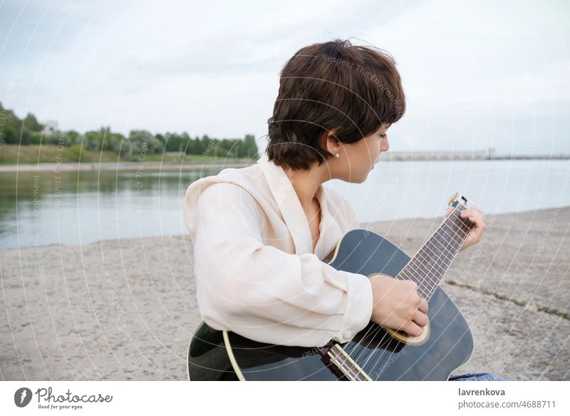 Junge Musikerin spielt Gitarre am Strand Spielen Klang spielen Frau Menschen Sitzen Gitarrenspieler Kaukasier jung Person Porträt Mädchen Instrument Ufer