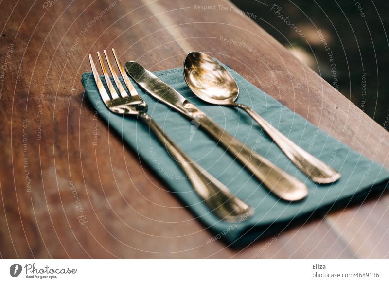 Goldenes Besteck auf blauer Stoffserviette auf einem Holztisch golden edel Restaurant Messer Gabel Löffel Tisch Serviette