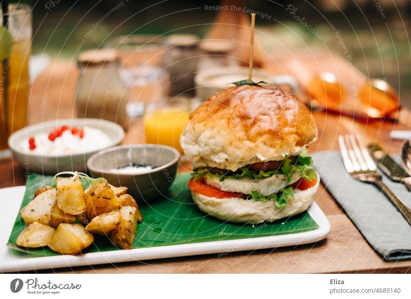 Burger mit Bratkartoffeln auf einem gedeckten Tisch im Restaurant bei Sonnenschein Fastfood Mittagessen Hamburger Mahlzeit lecker bunt frühstücksburger