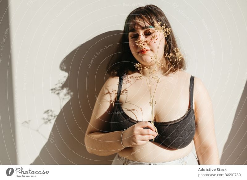 Übergewichtige Frau in Unterwäsche mit Trockenblumen Übergröße getrocknet Zweig Blume Figur Sonnenlicht Lächeln Dessous Raum genießen feminin Augen geschlossen
