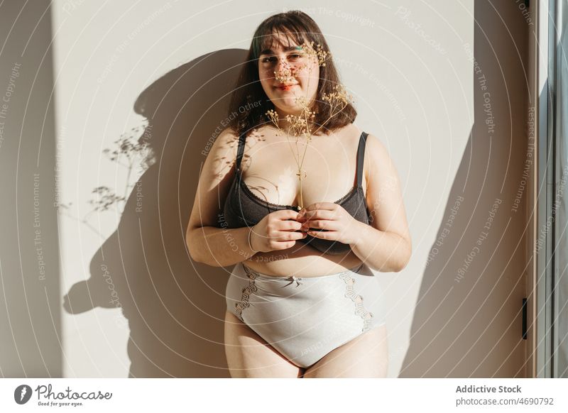 Übergewichtige Frau in Unterwäsche mit Trockenblumen Übergröße getrocknet Zweig Blume Figur Sonnenlicht Lächeln Dessous Raum genießen feminin Fenster Freude