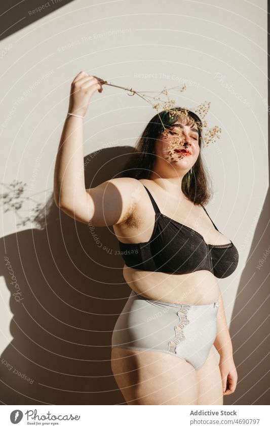 Übergewichtige Frau in Unterwäsche mit Trockenblumen Übergröße getrocknet Zweig Blume Figur Sonnenlicht Lächeln Dessous Raum genießen feminin Augen geschlossen