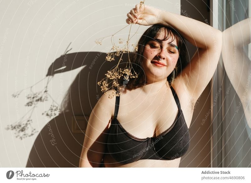Übergewichtige Frau in Unterwäsche mit Trockenblumen Übergröße getrocknet Zweig Blume Figur Sonnenlicht Lächeln Dessous Raum Schatten genießen feminin Make-up