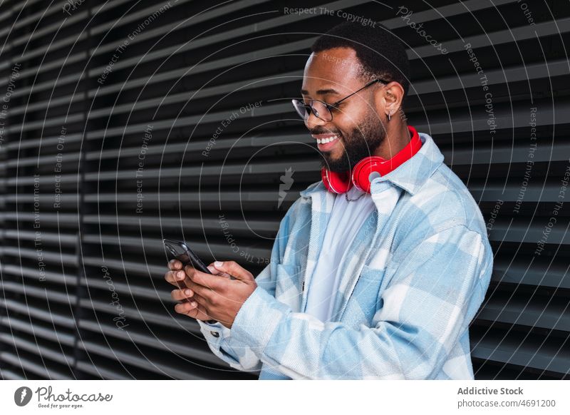 Fröhlicher schwarzer Mann mit Smartphone, der Musik hört Kopfhörer meloman Gesang Straße Großstadt Zeitvertreib Freizeit zuhören Gebäude Afroamerikaner