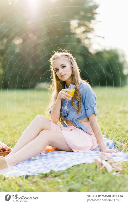 Porträt einer jungen Frau mit Orangensaft in einem Glas in einem Park. Person Decke Sitzen Glück Picknick Buch außerhalb Lächeln Fröhlichkeit hübsch Hut