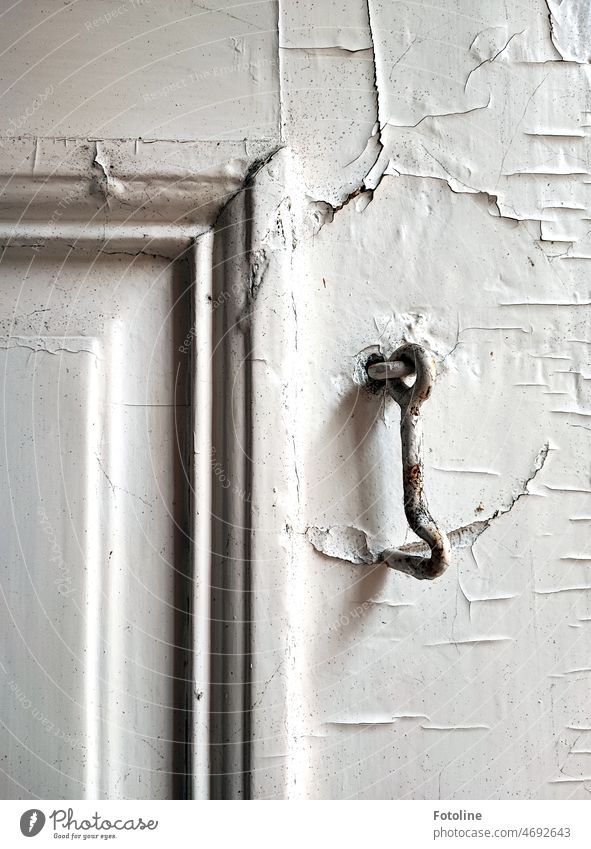 Der kleine Haken aus Metall hängt an einer alten verfallenen Tür. Seit vielen Jahren ist er schon arbeitslos, aber seine Arbeit hat Spuren an der Tür hinterlassen.