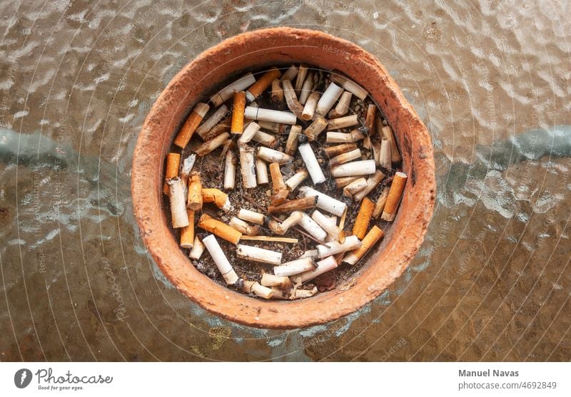 Aschenbecher mit verbrannten Zigarettenstummeln, aus Ton und auf einem Glastisch. Süchtige Sucht süchtig machend Anti-Raucher Aschenbecher Zigaretten Hintern